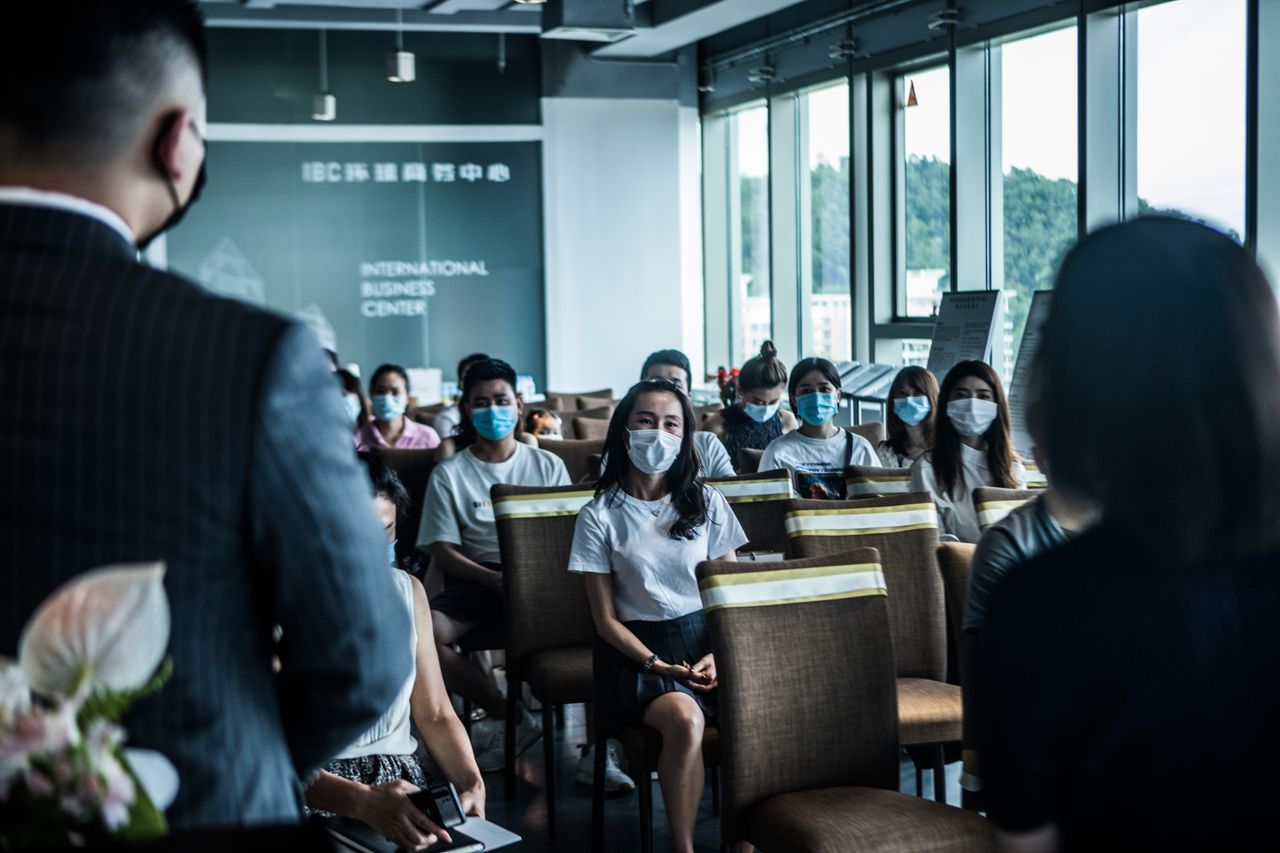 The Art of Drawing Readers In: Your attractive post title goes here Participants wearing face masks attending a business presentation in an indoor conference room.