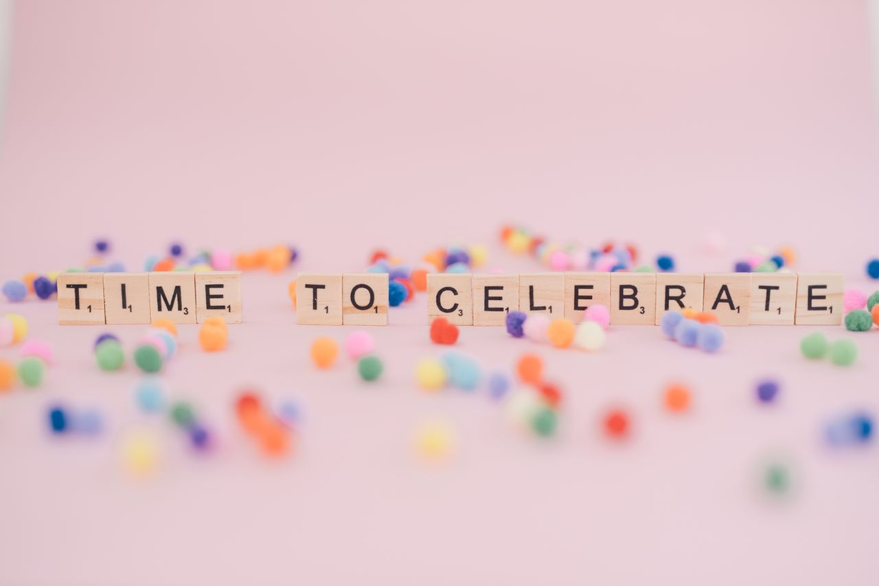 Services Colorful pom poms and alphabet tiles on pink background spelling 'Time to Celebrate.'